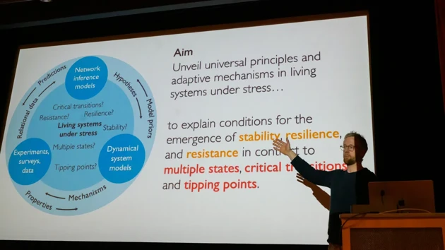 Martin Rosvall stands to the side of a large screen on which a slide is shown with images and text describing stress response modeling at IceLab