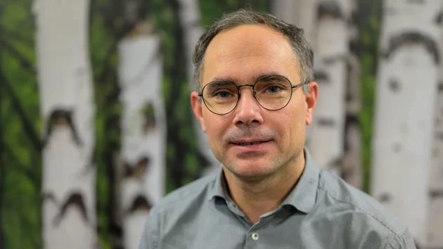 A man wearing glasses standing in front of a painting