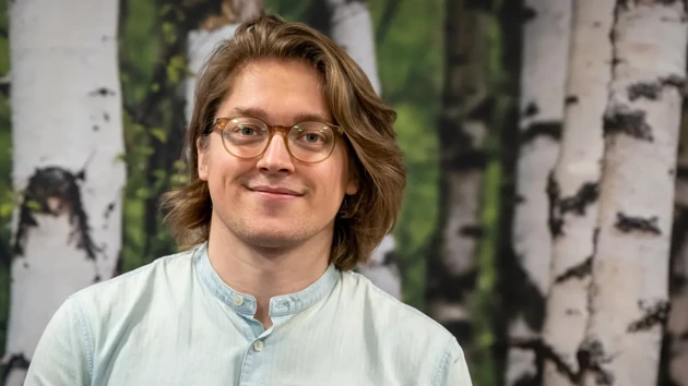 A man with glasses standing in front of a painting