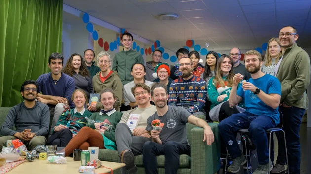 A group of people seated with holiday outfits, some on stools and some on a green couch