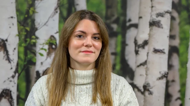 A woman standing in front of a painting of trees