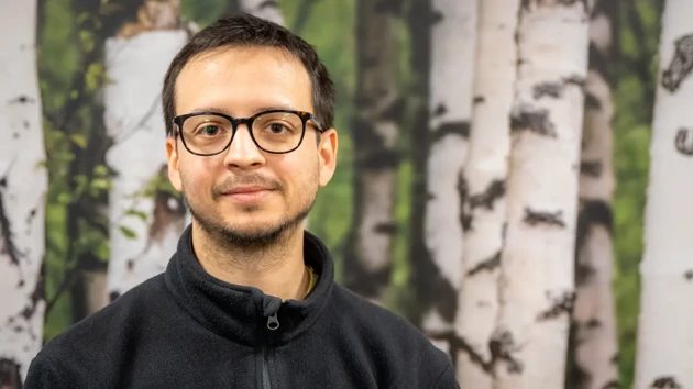 A man wearing glasses standing in front of a painting