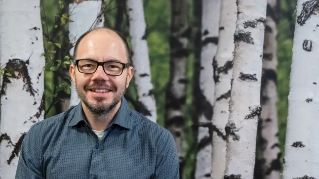 A man with glasses in front of birch trees