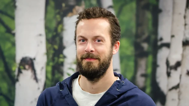 A man with a beard standing in front of a painting