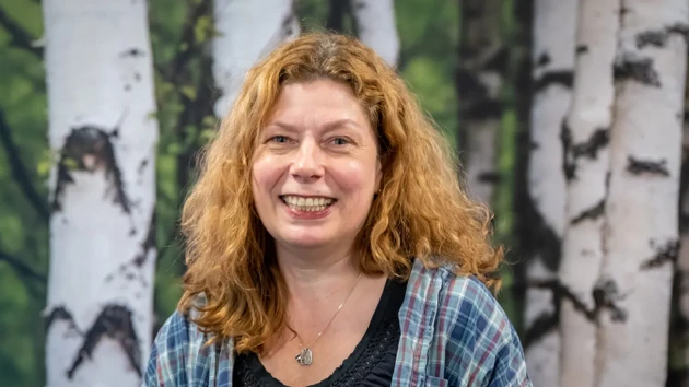 A woman standing in front of a painting of birch trees