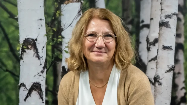 A woman sitting in front of a painting of trees