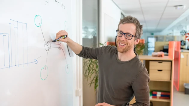 A man writes on a white board in an open office