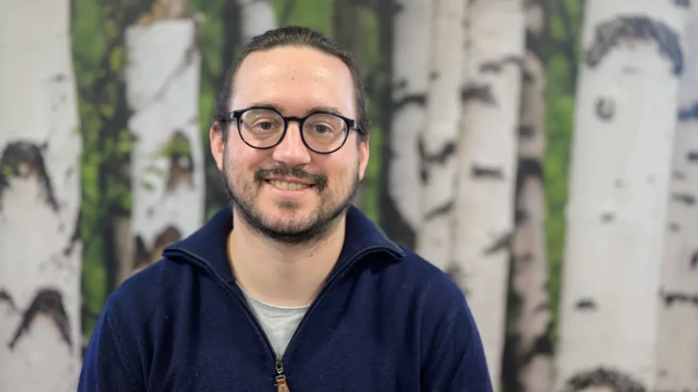 A man wearing glasses standing in front of a painting