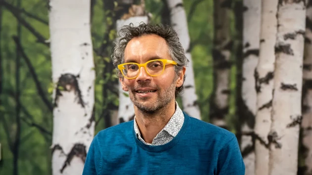 A man wearing glasses standing in front of a painting