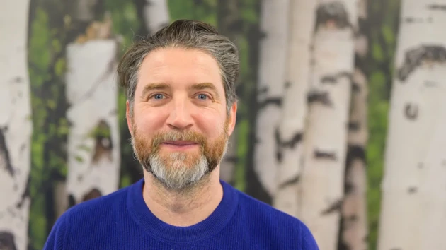 A man standing in front of a painting of birch trees