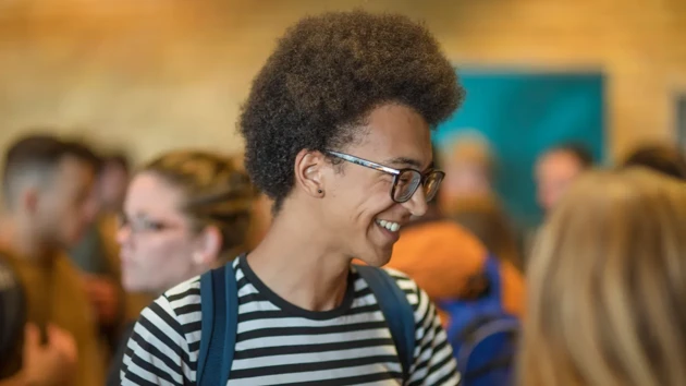 A smiling student in profile with a crowd of blurred out people around him.