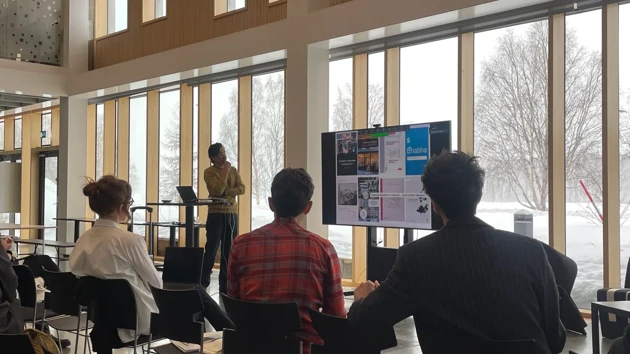 Person presenting in front of audiance in architecture school theatre space, windows, snow outside