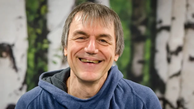 A man in a blue hoodie smiles at the camera