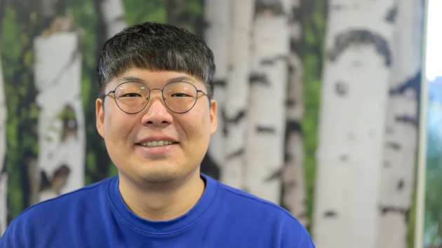 A man wearing glasses standing in front of a painting