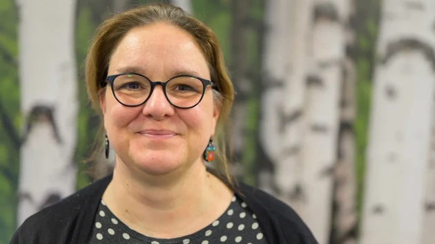 A woman wearing glasses standing in front of a painting