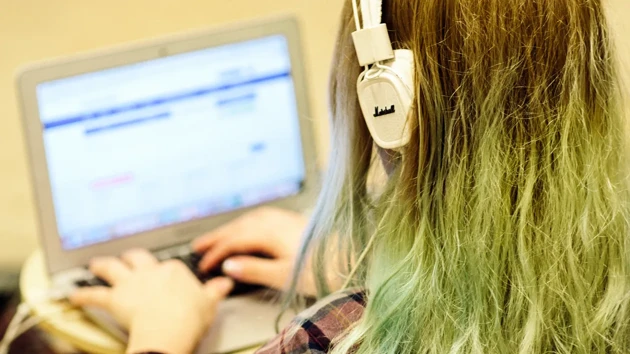 A woman is typing on a computer with headphones on her head.