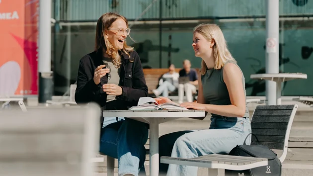 Two smiling students sitting at an outdoor table on campus.