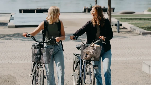 Två kvinnor leder varsin cykel och samtalar.