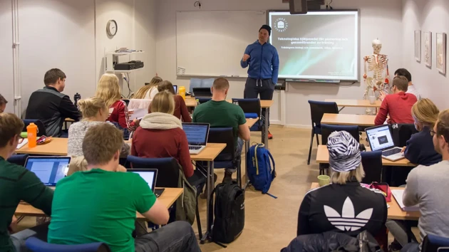 A classrom with students sitting with their back to the camera and a male teacher stood at the front.