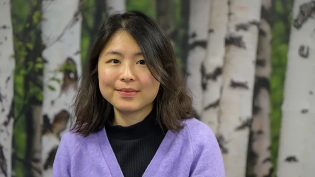 A woman standing in front of a painting of trees